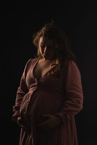 Stimmungsvolles Schwangerschaftsportrait im Studio mit dunklem Hintergrund und ausdrucksstarkem Licht in Kiel