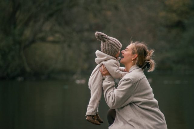 Lebendiges Familienfoto in Kiel: Mutter schaukelt lachend ihre kleine Tochter unter freiem Himmel im Park