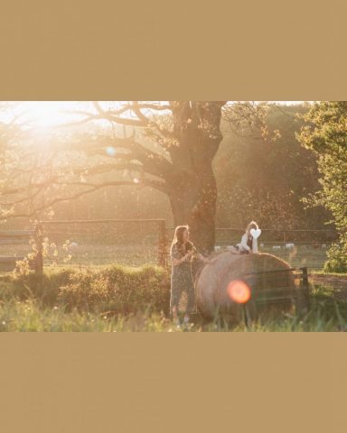 Lachende Mutter schaut zu ihrer Tochter auf dem Heuballen, warmes Licht des Sonnenuntergangs – Familienfotoshooting am Stadtrand von Kiel