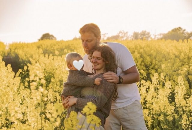 Familienportrait mit Vater, Mutter und Baby stehend im Rapsfeld bei Sonnenuntergang in Kiel