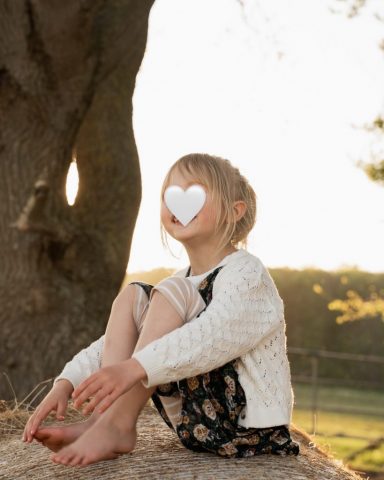 Lachendes Portrait der kleinen Tochter auf einem Heuballen – Familienfotoshooting in Kiel im warmen Abendlicht