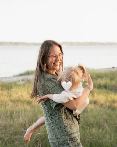 Lachende Mutter hält ihre kleine Tochter im Arm – Familienfotoshooting am Strand in Kiel bei Abendlicht