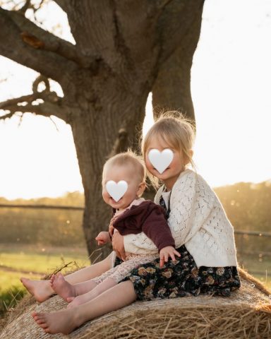 Zwei Schwestern kuscheln auf einem Heuballen im warmen Gegenlicht – Familienfotoshooting in Kiel