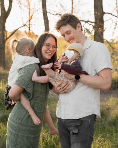 Junge Familie beim Spaziergang im Kieler Park, Baby auf dem Arm, stimmungsvolles Abendlicht