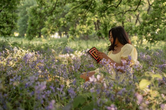Junge Frau sitzt zwischen lila Blumen auf einer Wiese und liest ein Buch im Abendlicht – Portraitfotoshooting in Kiel