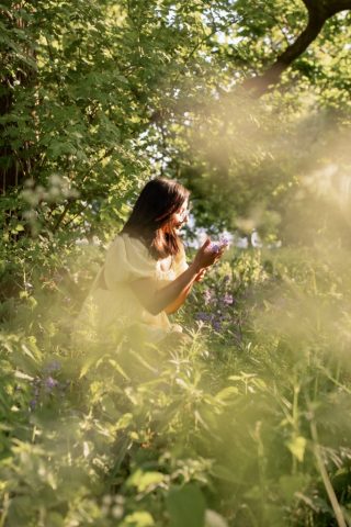 Junge Frau im Abendlicht auf einer Wiese mit lila Blumen unter Bäumen – Portraitfotoshooting in Kiel