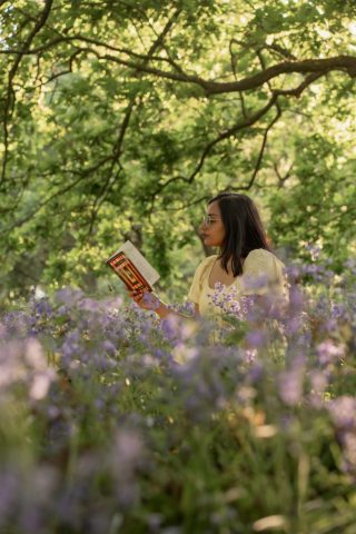 Frau vertieft sich in ein Buch auf einer blühenden Wiese mit violetten Blumen im Sonnenuntergang – Portraitaufnahme in Kiel