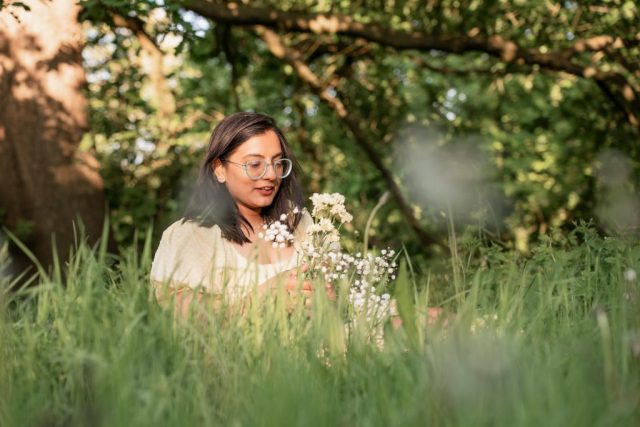 Junge Frau sitzt im Gras auf einer Wiese in Kiel und hält weiße Blumen in der Hand – Portrait im Abendlicht
