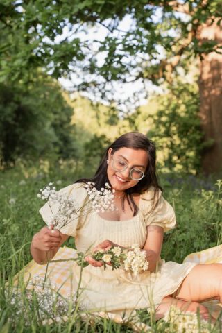 Portrait einer Frau im goldenen Abendlicht, sitzend im Gras mit weißen Blumen – Outdoor-Fotoshooting in Kiel