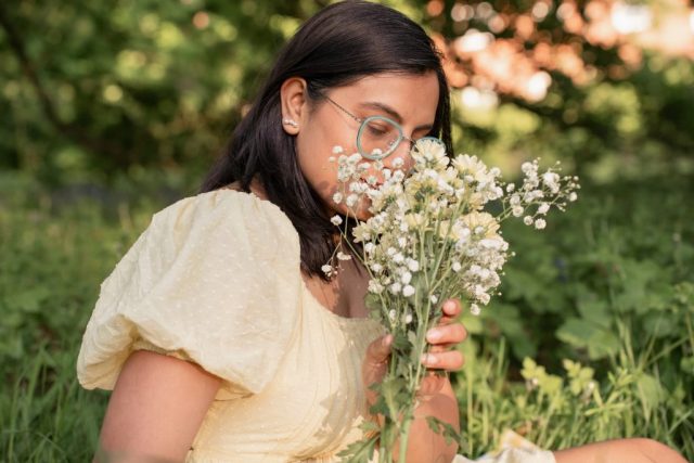 Stimmungsvolle Portraitaufnahme: Frau sitzt im Gras mit Blumen in der Hand im warmen Sonnenuntergang – aufgenommen in Kiel