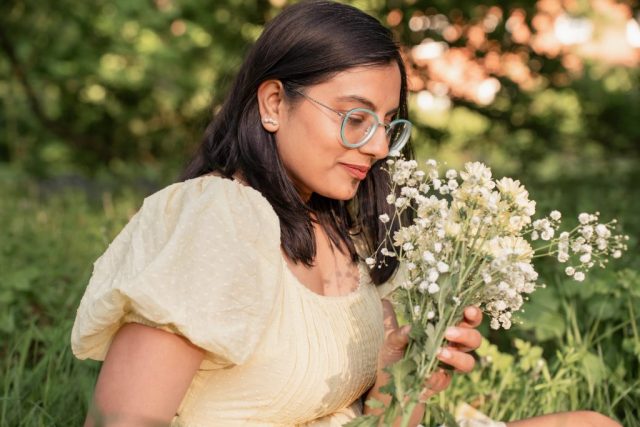 Frau hält zarte Blumen in der Hand und sitzt entspannt im Gras unter Bäumen – Portraitfotoshooting bei Abendlicht in Kiel
