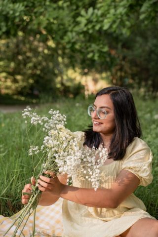 Junge Frau genießt den Moment im Gras sitzend, mit Blumen in der Hand und weichem Sonnenlicht – Portraitfotografie in Kiel