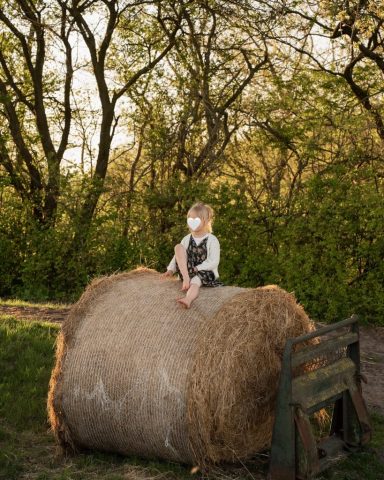 Lebendige Aufnahme eines lachenden Mädchens auf einem Heuballen, warmes Abendlicht – Familienfotoshooting Kiel