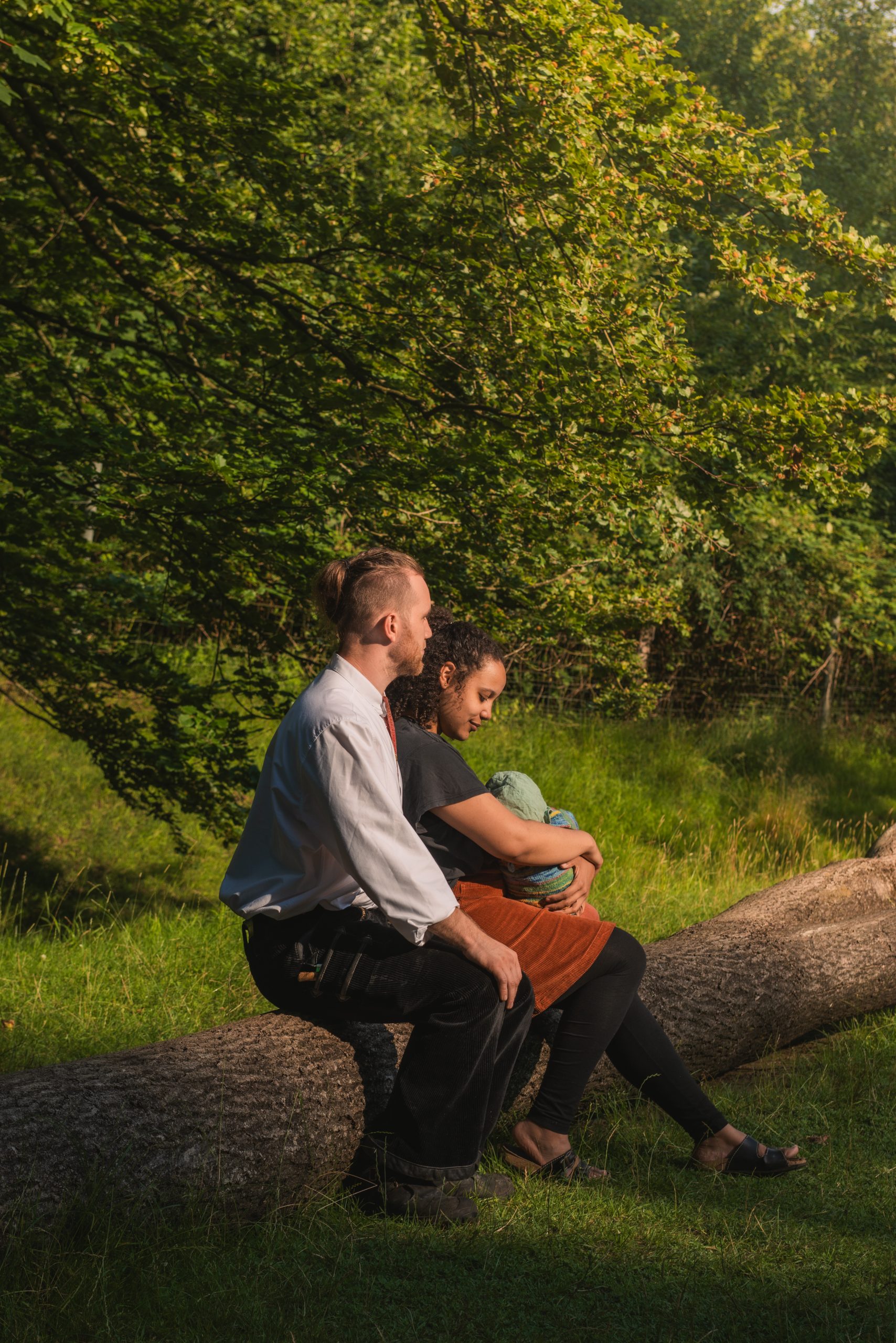 Eltern und ihr Baby sitzen gemeinsam auf einer Wiese im Park im stimmungsvollen Abendlicht in Kiel