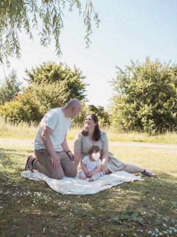 Familie sitzt gemütlich auf einem Leinentuch am Boden im Park – natürliches Fotoshooting in Kiel