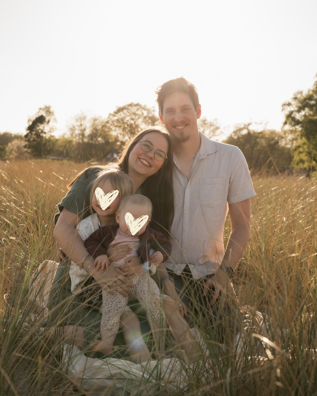 Familienfoto im Abendlicht in Kiel: Vater, Mutter und ihre zwei kleinen Töchter sitzen gemeinsam im Gras und genießen den Moment miteinander