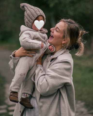 Fröhlicher Familienmoment in Kiel: Mutter hält ihre kleine Tochter lachend hoch am Seeufer im Park