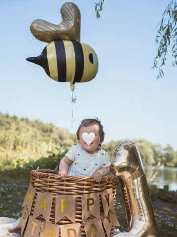Fröhliches Geburtstagsfoto: Kleines Mädchen im Korb, dekoriert mit Ballon und Girlande – aufgenommen im Park in Kiel