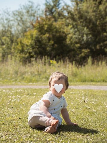 Mädchen sitzt fröhlich auf der Wiese im Park – natürliche Aufnahme in Kiel