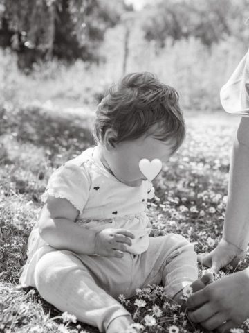Familienmoment im Park: Mädchen sitzt auf der Wiese und erhält eine Blume von der Mutter – Fotoshooting in Kiel