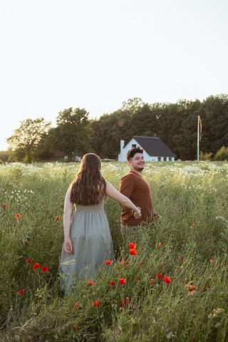 Zwei Menschen halten sich an den Händen, umgeben von wildem Blumenmeer bei Abendlicht
