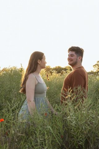 Paar steht im grünen Blumenfeld und schaut sich liebevoll im warmen Licht des Sonnenuntergangs an
