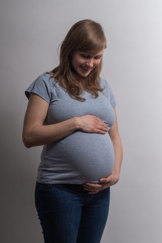 Ruhiger Moment einer werdenden Mutter, die liebevoll ihren Babybauch hält – Studioaufnahme