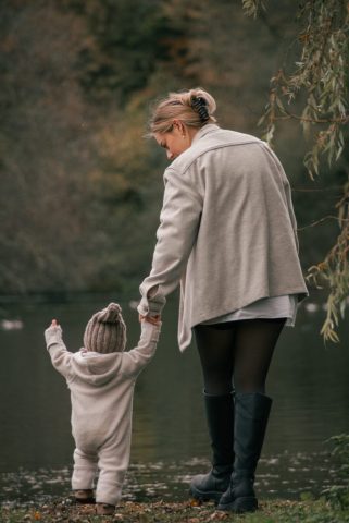 Mutter spaziert im Park am See in Kiel mit ihrer kleinen Tochter und hält sie liebevoll an der Hand